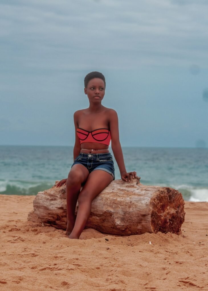 Woman in red bandeau top and denim shorts on a beach log