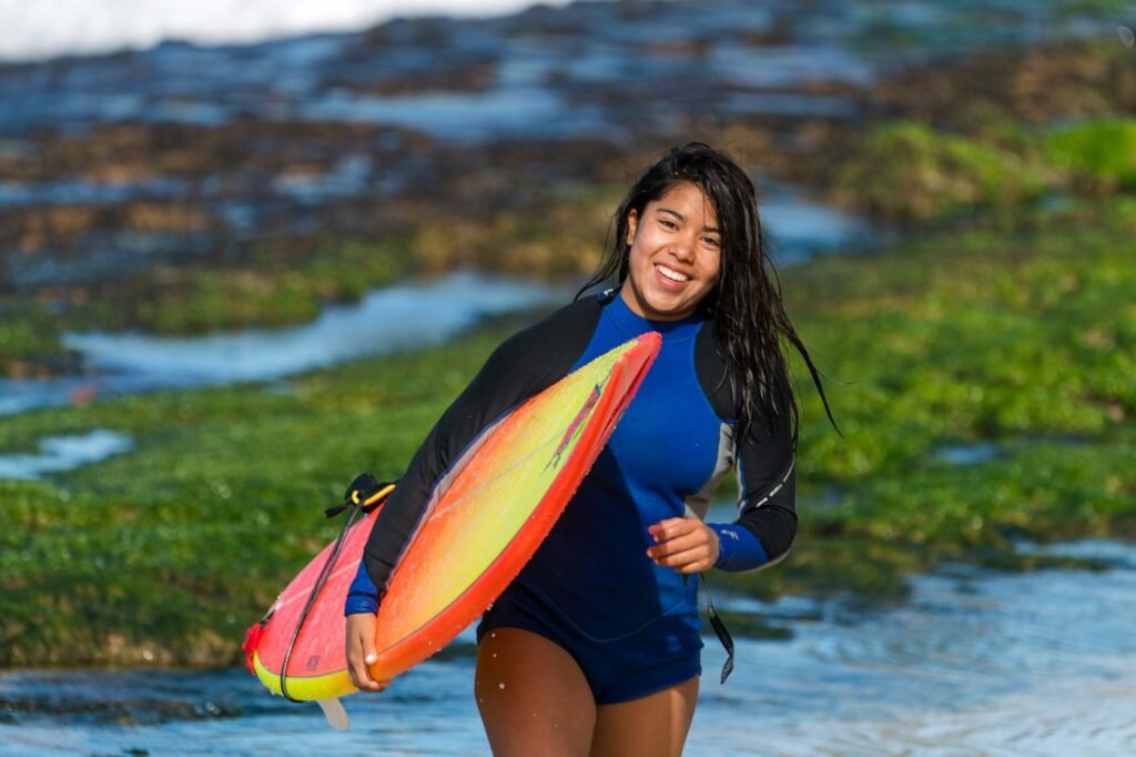 Smiling woman in blue rash guard carrying a surfboard